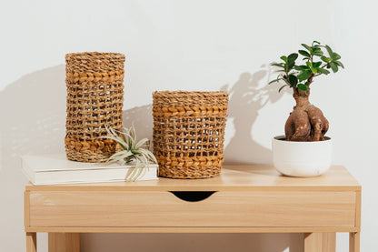 Short and tall brown woven vase with glass inserts on brown table.