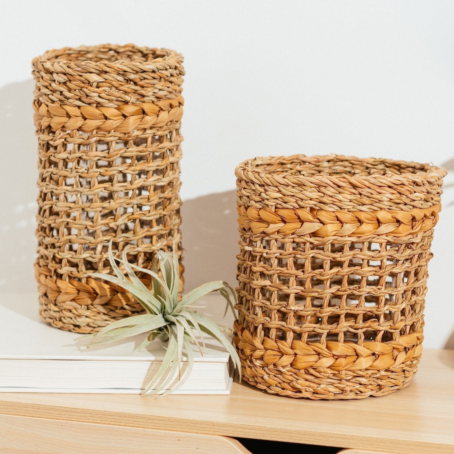 Short and tall brown woven vase with glass inserts on wood table.