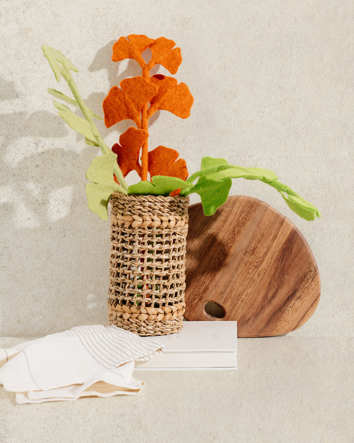 Tall brown woven vase with glass insert and orange flowers on white cloth.