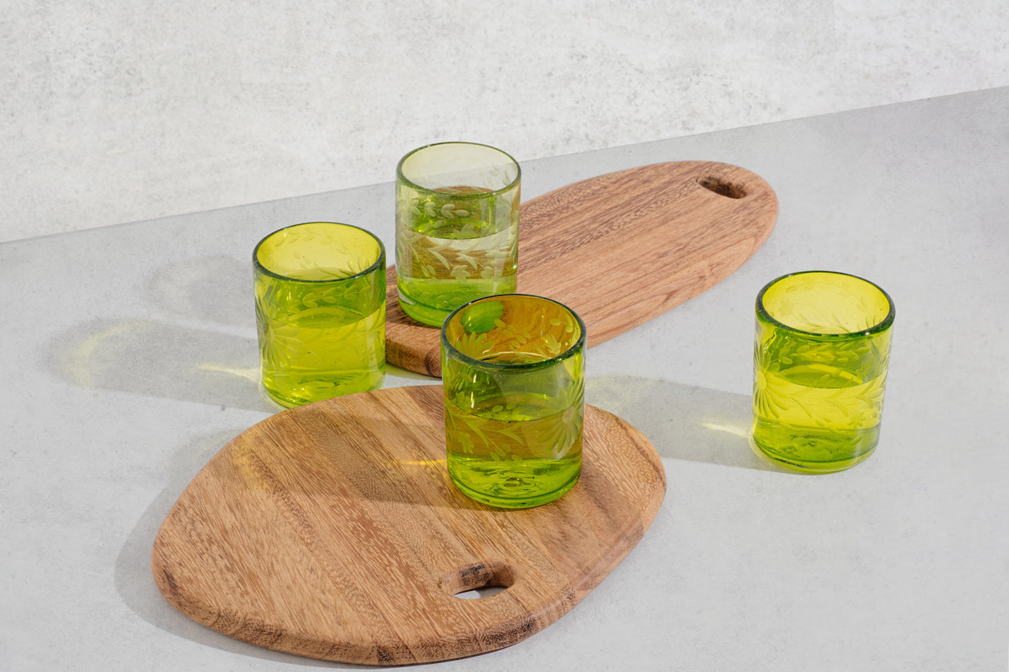 Brown wood oval serving board, scattered green glasses and round serving board in front.