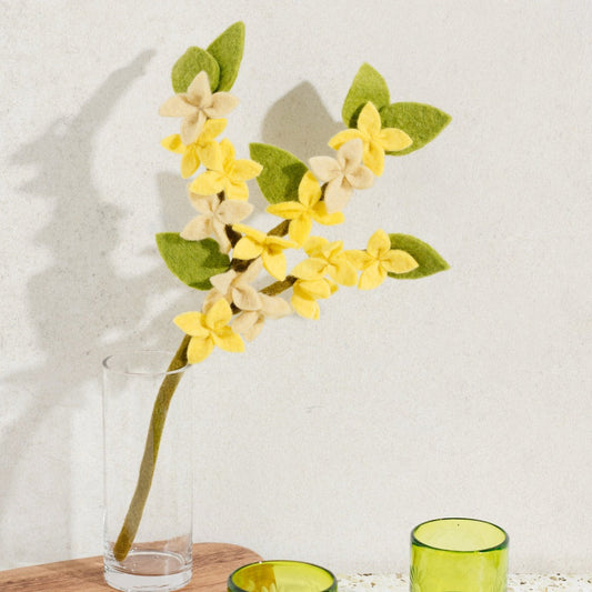 Felt yellow Forsythia flower with three branches on stem in glass vase.