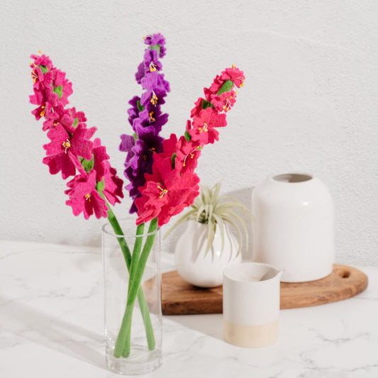 Three felt Crepe Myrtle flowers in magenta, purple, and hot pink in a glass vase.