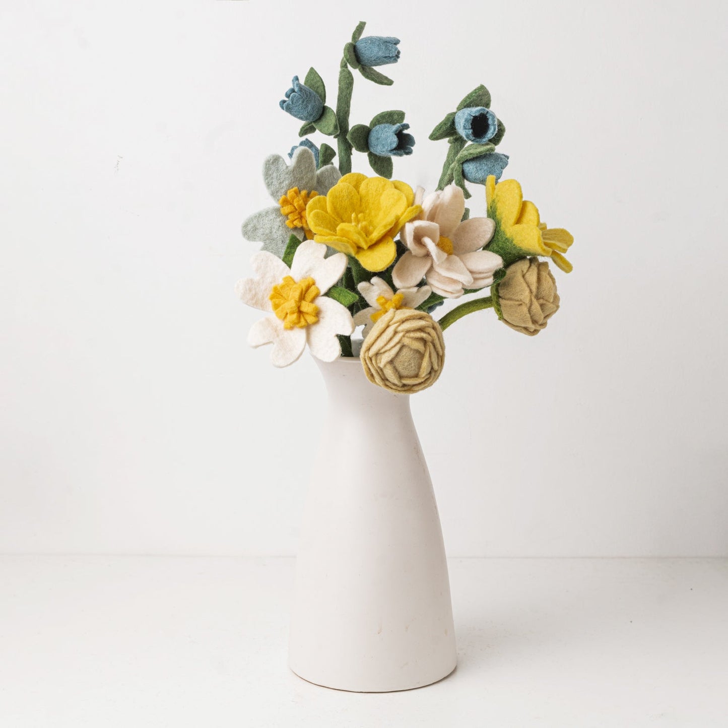 Blue, yellow, and white flower felt floral arrangement in a white vase.
