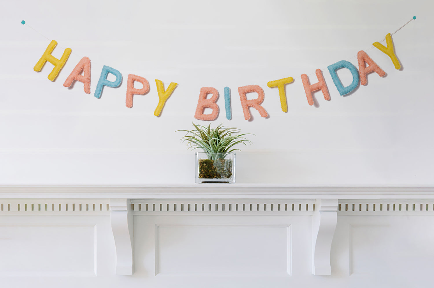 Felt garland spelling Happy Birthday in pastel yellow, pink, and blue colors hanging over mantel.