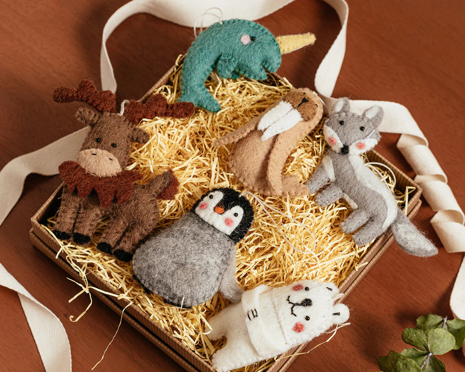 Felted wool ornaments of a narwal, walrus, fox, moose, penguin, and polar bear in a box.