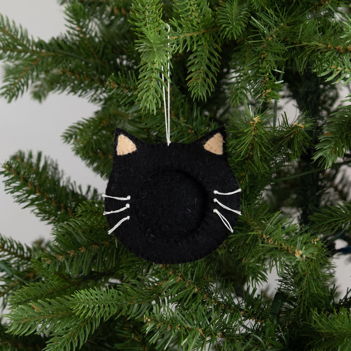 Felt ornament of a black cat face outline with a frame in the middle to put a photograph, hanging on a Christmas tree.
