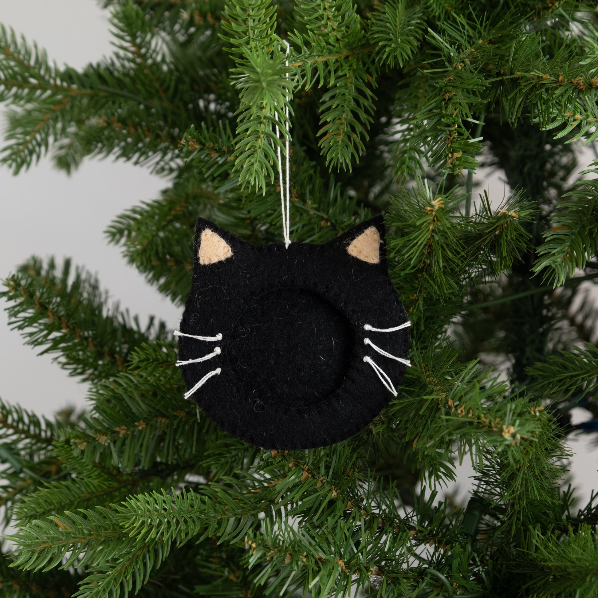 Felt ornament of a black cat face outline with a frame in the middle to put a photograph, hanging on a Christmas tree.