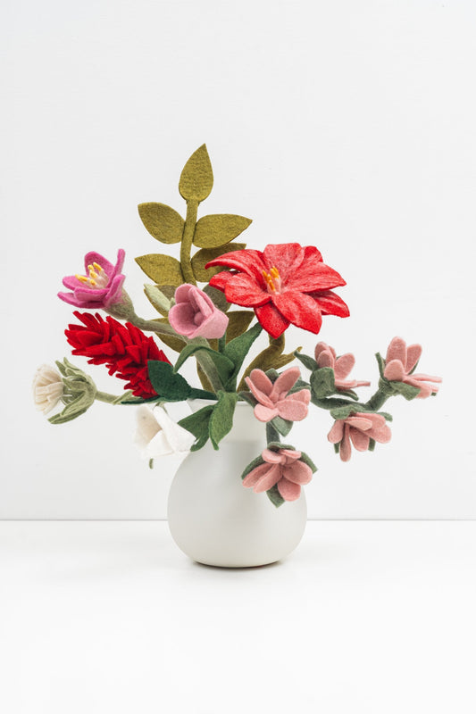 Bouquet of pink, red, and white felt flowers and green leaves in a white vase.
