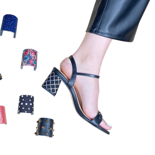 Woman's right foot and leg wearing black pants and black sandal with silver accents across toe strap and on heel. Multiple heel clips are shown, including blue, floral, silver diamond pattern, silver dot pattern, red, black with metal.