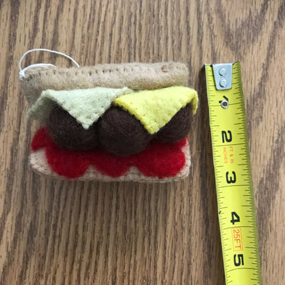 Felt ornament of meatball sub sandwich measuring about 2.5 inches wide.