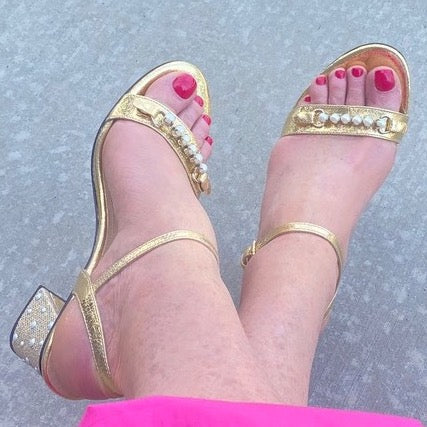 Looking down at pair of feet wearing gold sandal with pearl toe strap and heel cover.