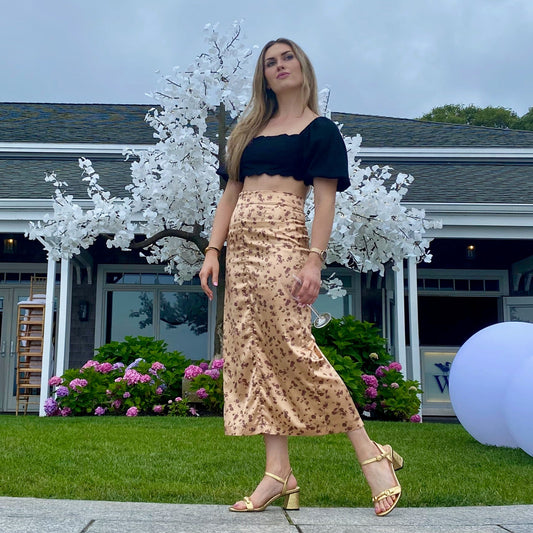 Woman in black shirt and floral skirt wearing gold sandal.