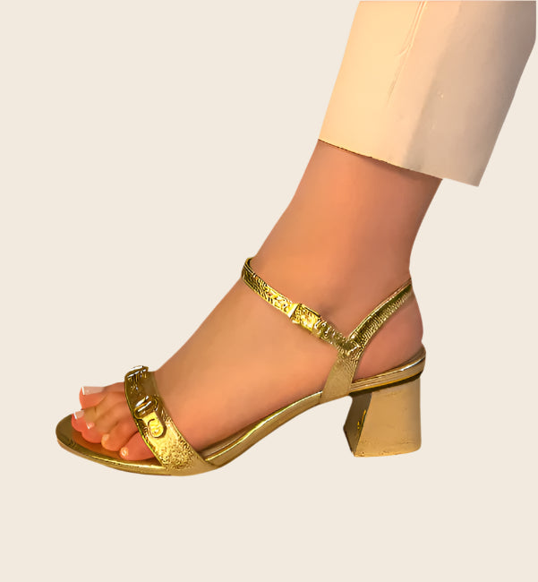 Closeup of woman's left leg and foot, wearing white pants and gold sandal.