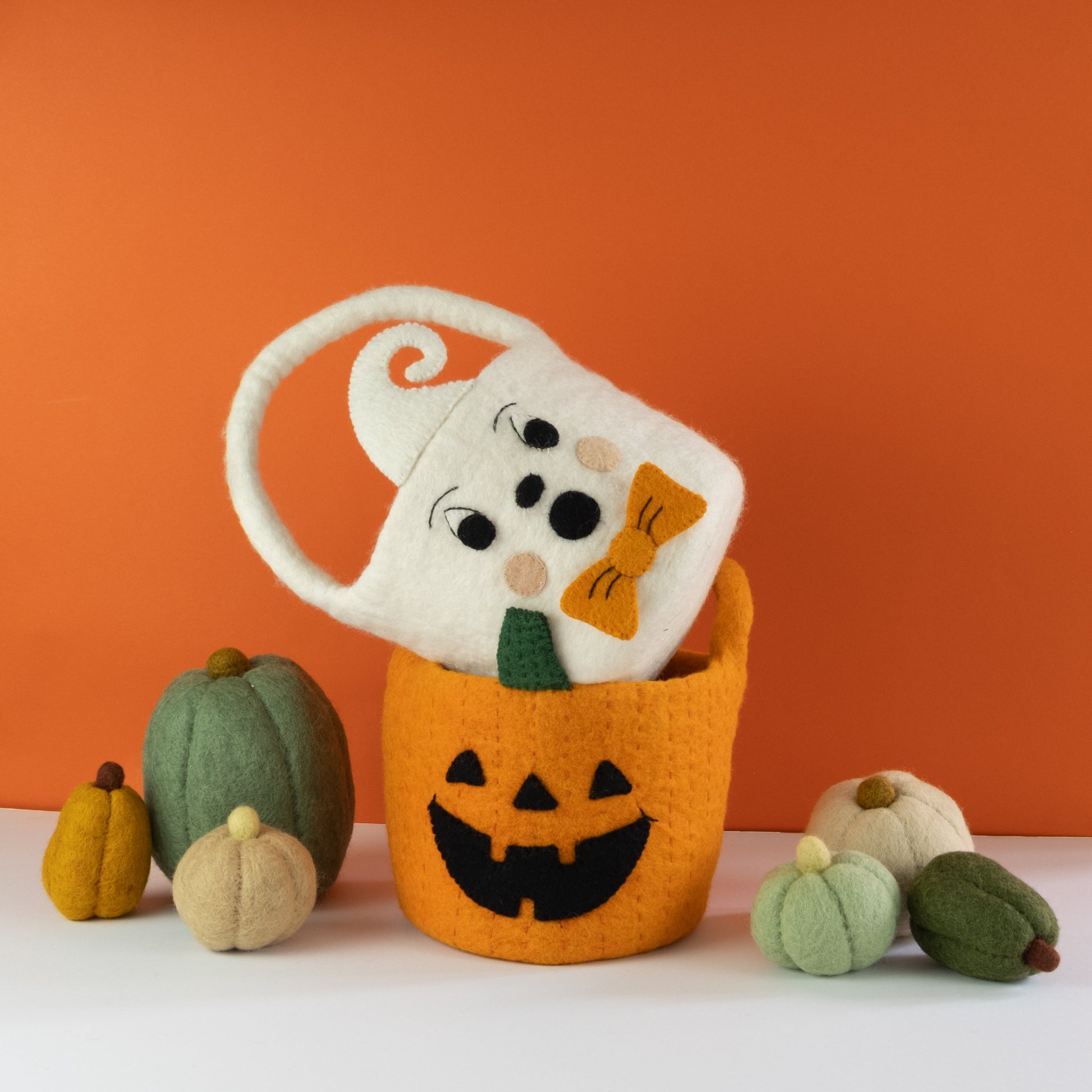 Orange felt jack-o-lantern trick-or-treat bucket and a white felt ghost trick-or-treat bucket with orange bow tie on top and felt pumpkins beside them.