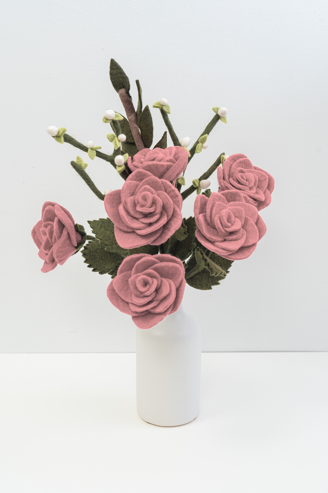 Felt flower bouquet of pink roses and white buds in a white vase with white background.