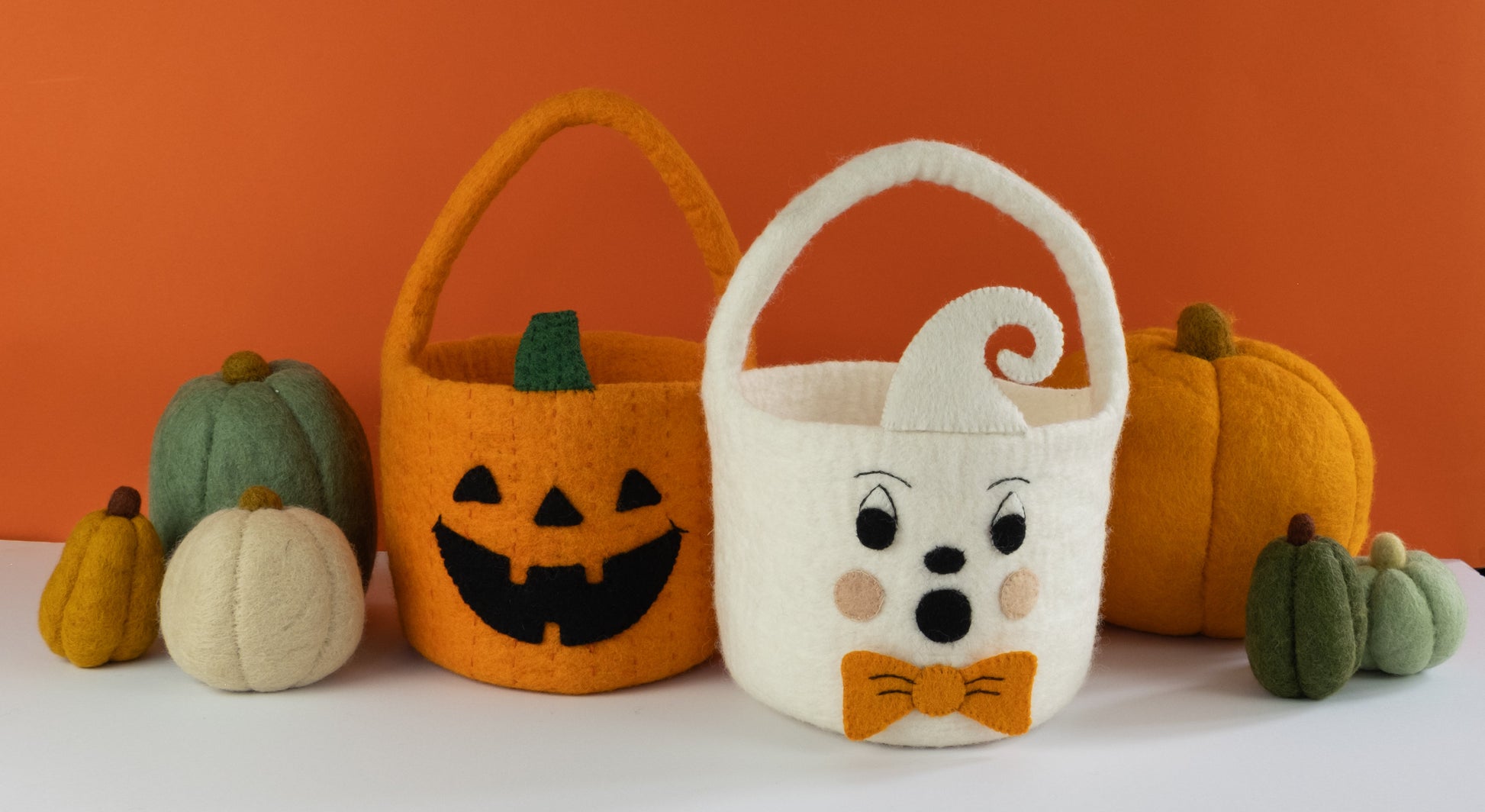 Orange felt jack-o-lantern trick-or-treat bucket and a white felt ghost trick-or-treat bucket with orange bow tie and felt pumpkins behind them.
