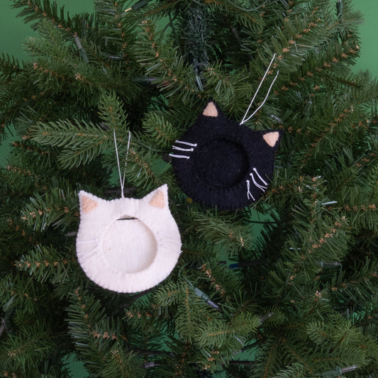 Felt ornaments of one black and one white cat face with a frame in the middle to put a photograph hanging on a Christmas tree.