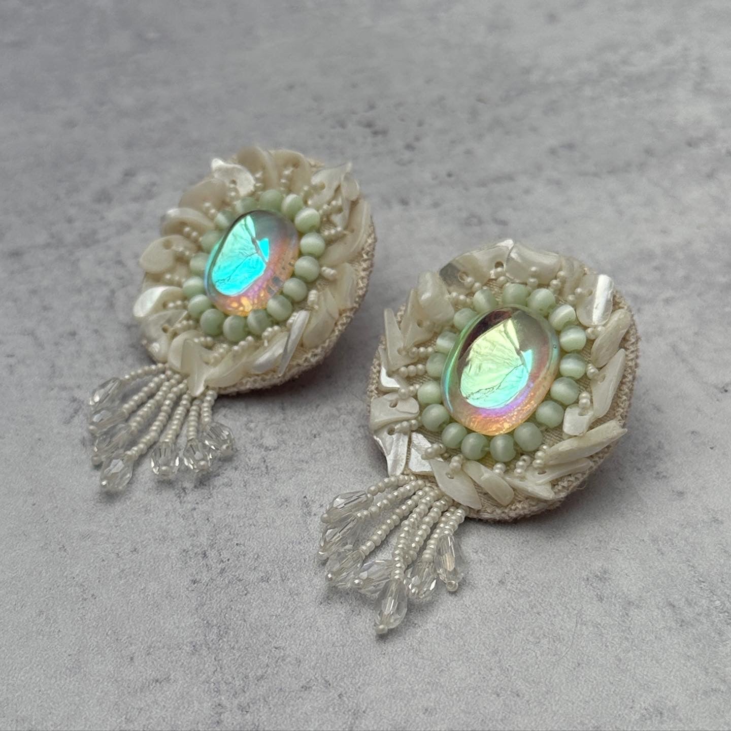 Pair of iridescent white earrings with pink and blue accents on grey background.
