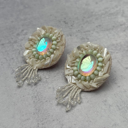 Pair of iridescent white earrings with pink and blue accents on grey background.