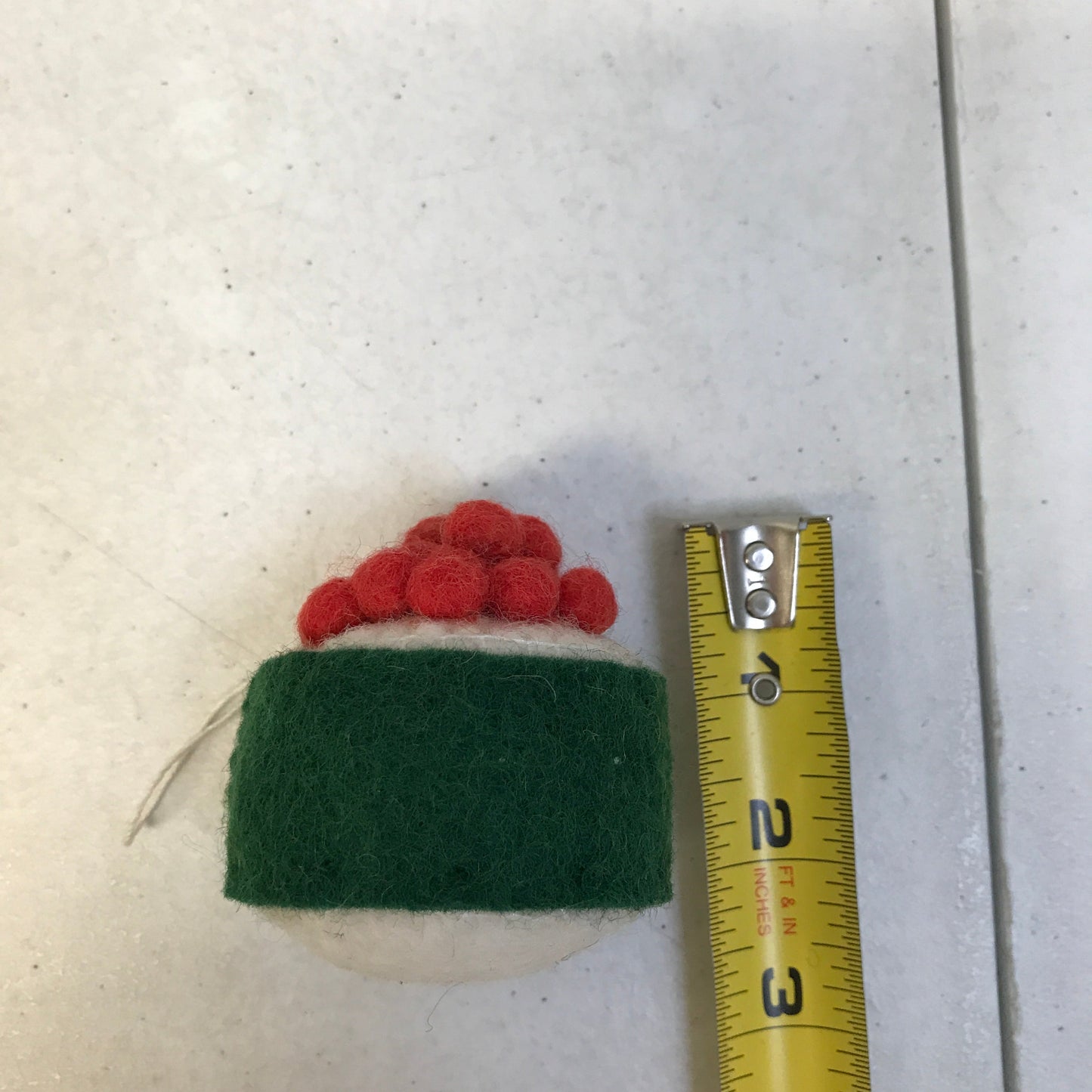 Felt ornament of sushi with salmon roe on top next to measuring tape that shows it is 2 inches tall.
