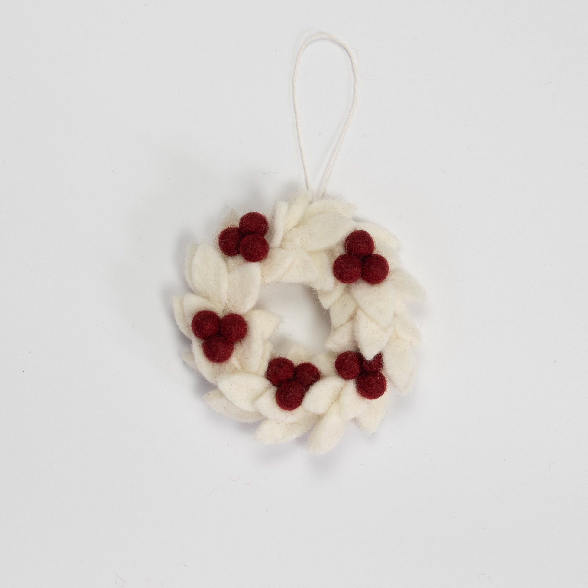 Felt ornament of a mini wreath in white with red berries.