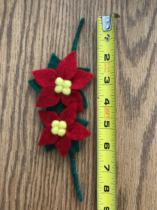 Red poinsettia flower felt gift topper with green leaves next to measuring tape showing the flowers to be approximately 4.5 inches lengthwise.