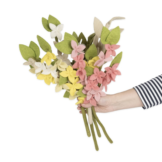 A hand holding out a bunch of yellow, pink, and white felt Forsythia flowers.