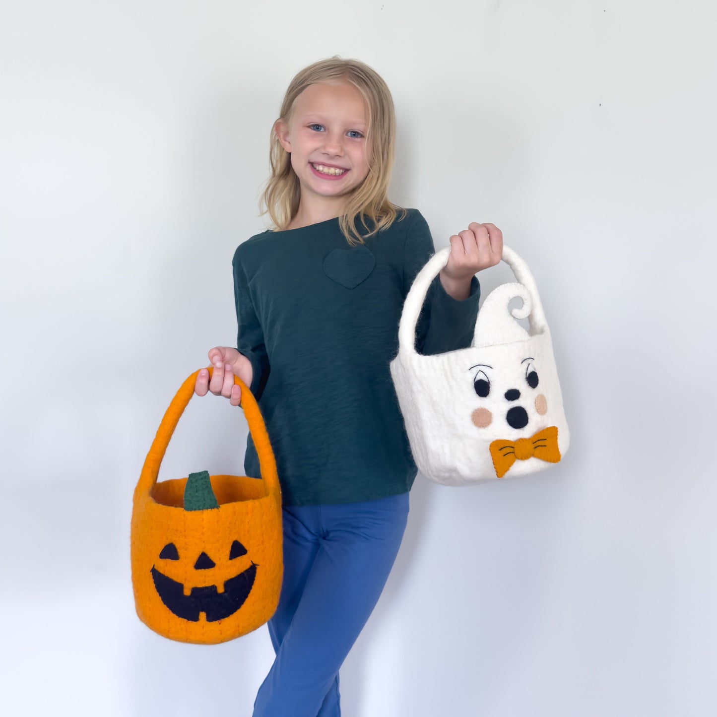 Blond girl holding orange felt jack-o-lantern trick-or-treat bucket and a white felt ghost trick-or-treat bucket with orange bow tie.