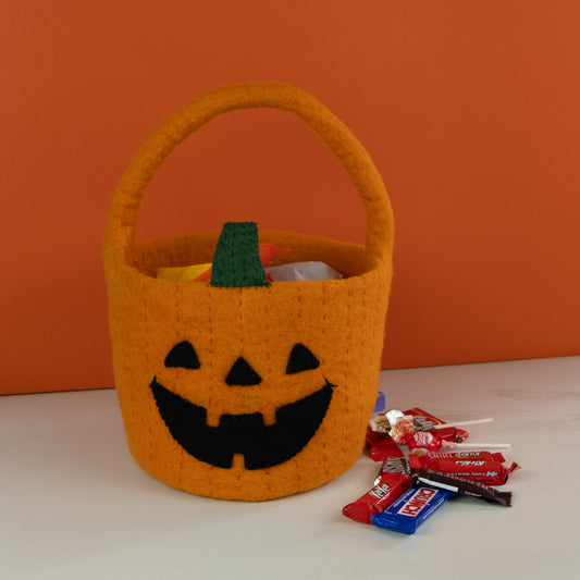 Orange felt jack-o-lantern trick-or-treat bucket with candy in and around it.