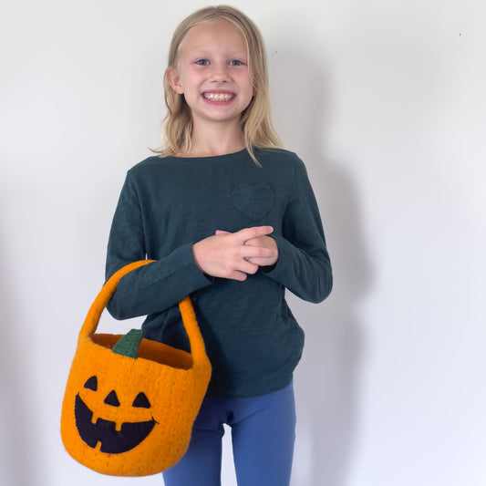 Blond girl holding an orange felt jack-o-lantern trick-or-treat bucket.