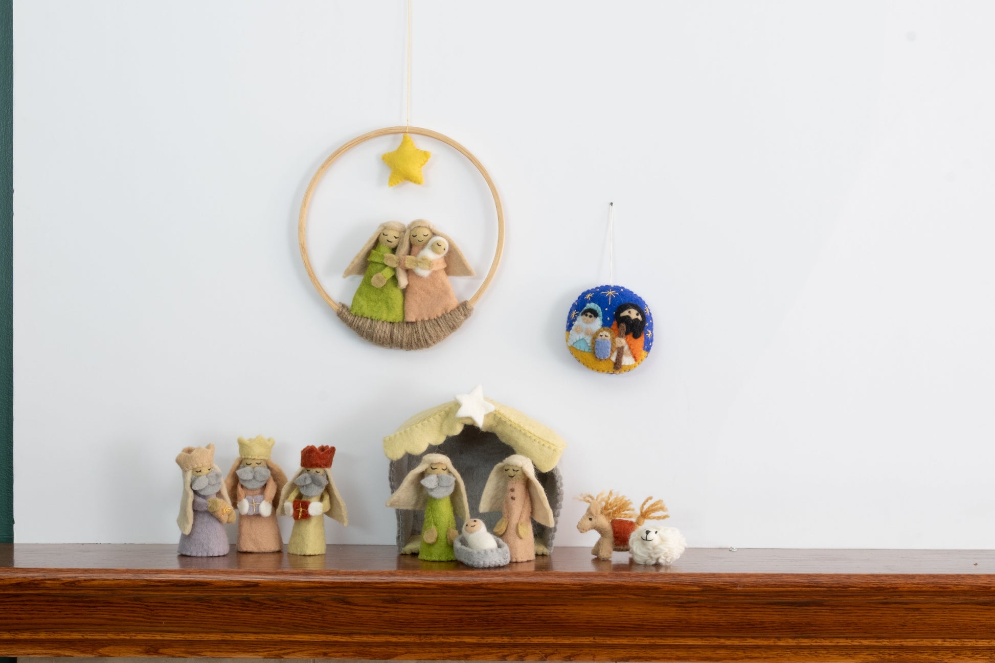 Felt ornament in a circle shape showing the nativity scene of Mary, Joseph, and baby Jesus underneath the night sky behind a full nativity scene set.