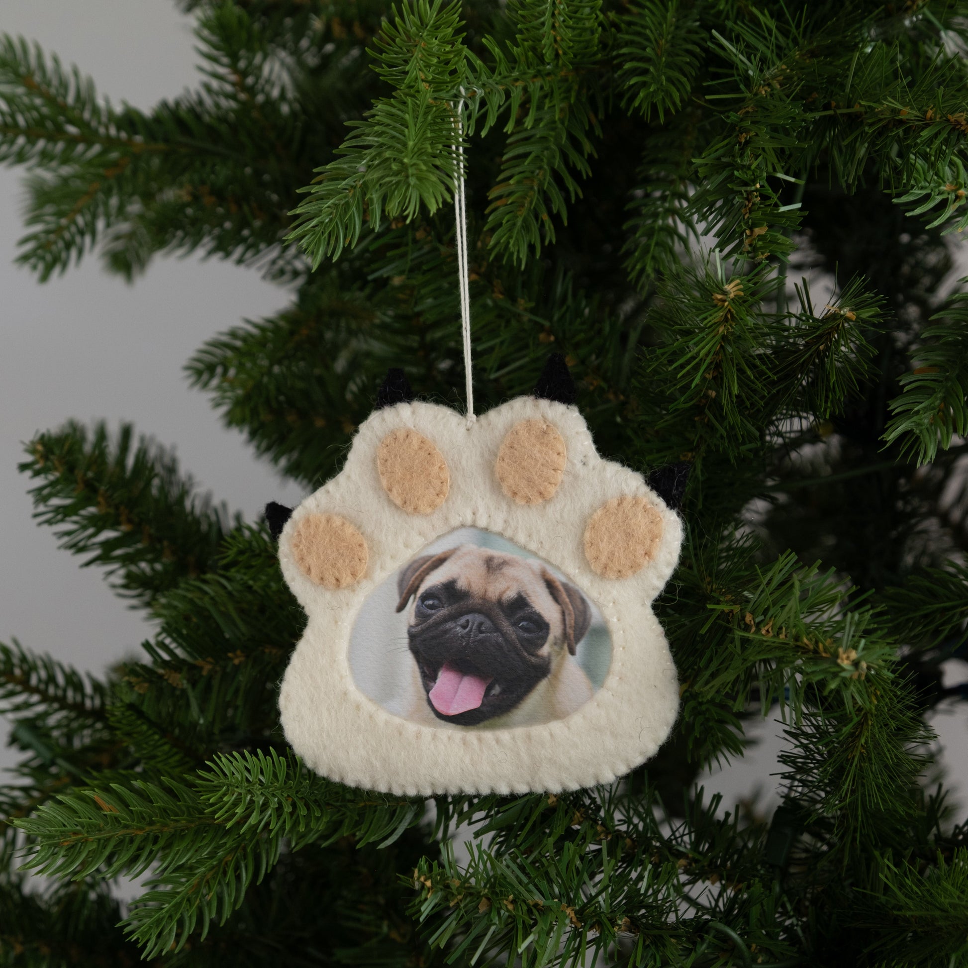 Felt ornament of a white paw print with a picture frame in the middle with a pug dog picture.