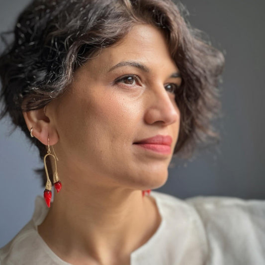 Right front view of woman wearing red and gold double chili pod earrings with silver colored findings.