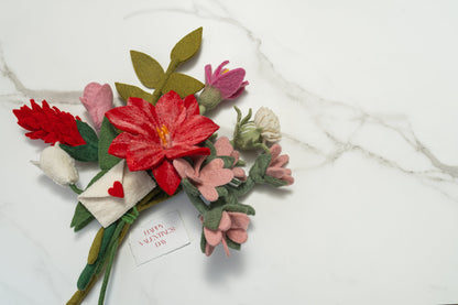 Bouquet of pink, red, and white felt flowers and green leaves on marble surface.