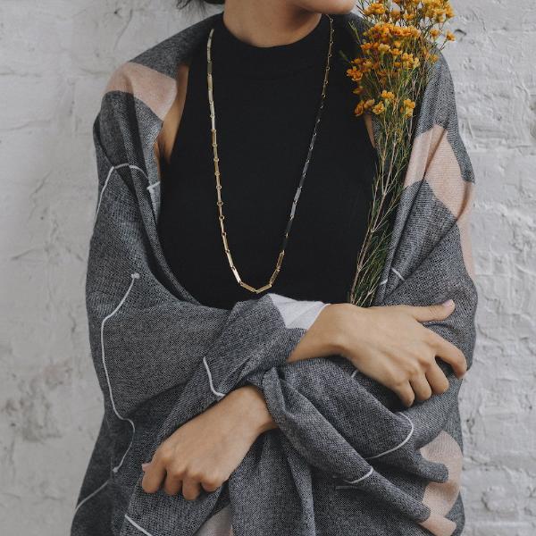 Close up of white, gold, and black link necklace on a woman in a black dress and grey shawl.