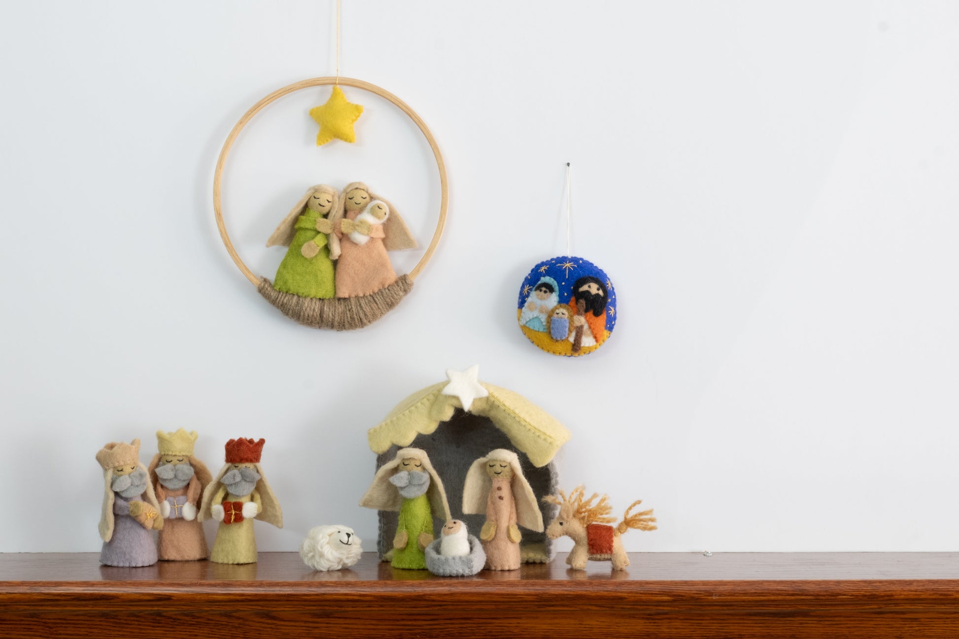 Felt ornament in a circle shape showing the nativity scene of Mary, Joseph, and baby Jesus underneath the night sky behind a full nativity scene set.