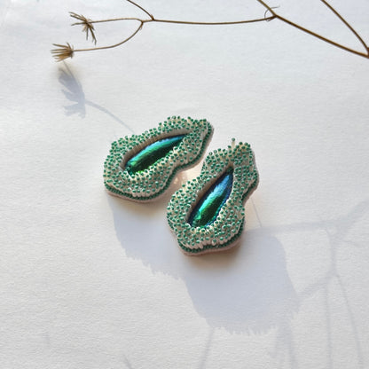Pair of Pennata beaded green glass earrings with iridescent centers and a branch above.