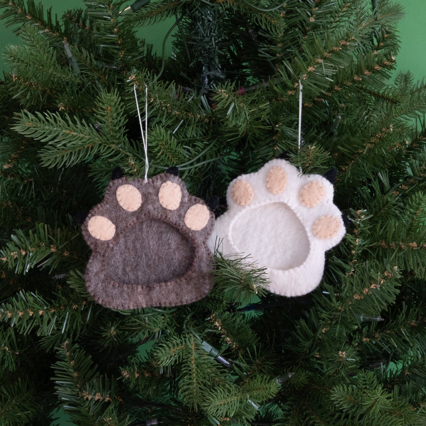 Felt ornaments of one brown and one white pawprint with a frame in the middle hanging on a tree.