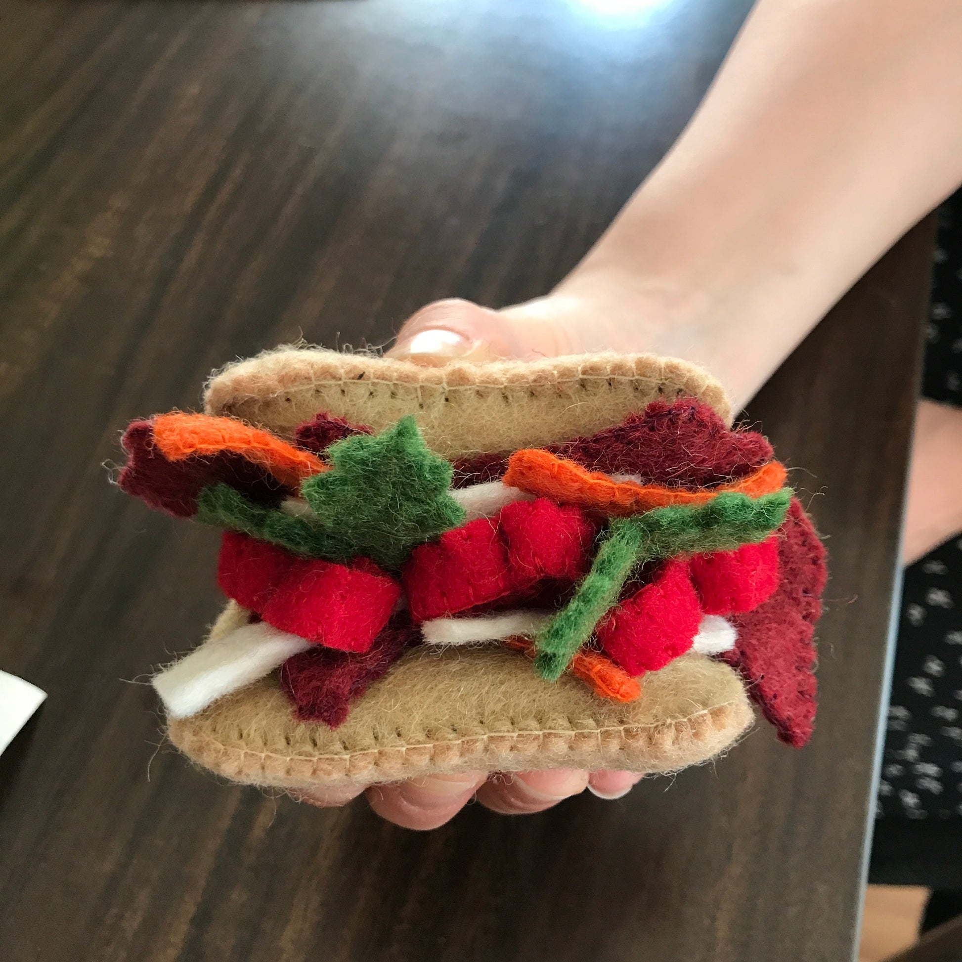 Close up of felt ornament of a Banh Mi sandwich being held in a hand.