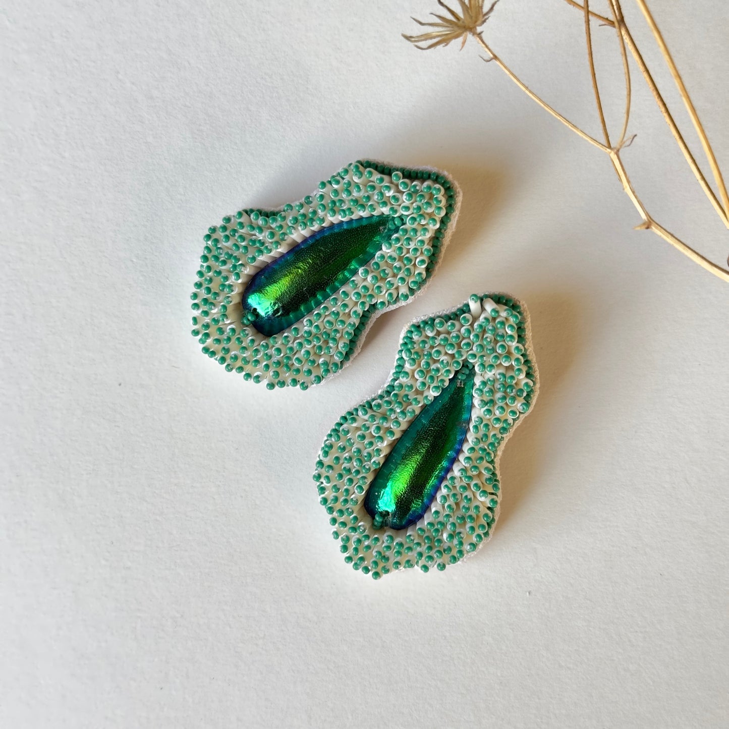 Pair of Pennata beaded green glass earrings with iridescent centers and a twig in top right corner.