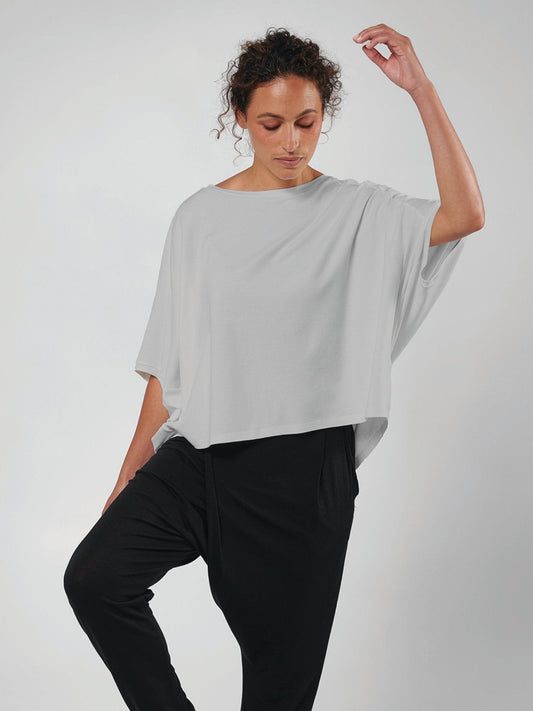 Woman wearing a light gray oversized shirt over a black outfit on a white background.