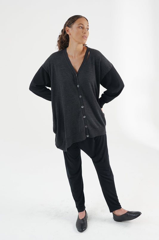 Front view of woman wearing Woman wearing charcoal/black cardigan with black pants and shoes. Hands are on her back and left toes pointed in the air.