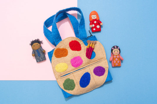 Felt art palette with colorful paint swatches, felt artist puppet dolls of Yayoi Kusama, Frida Kahlo, and Jean-Michel Basquiat, and felt paintbrushes on a two-tone pink and blue background. Fair Trade & handmade kids gift | Global Goods Partners
