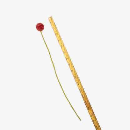 Handmade fair trade floral stem with red bloom and green leaves next to a ruler for scale on a white background | Global Goods Partners