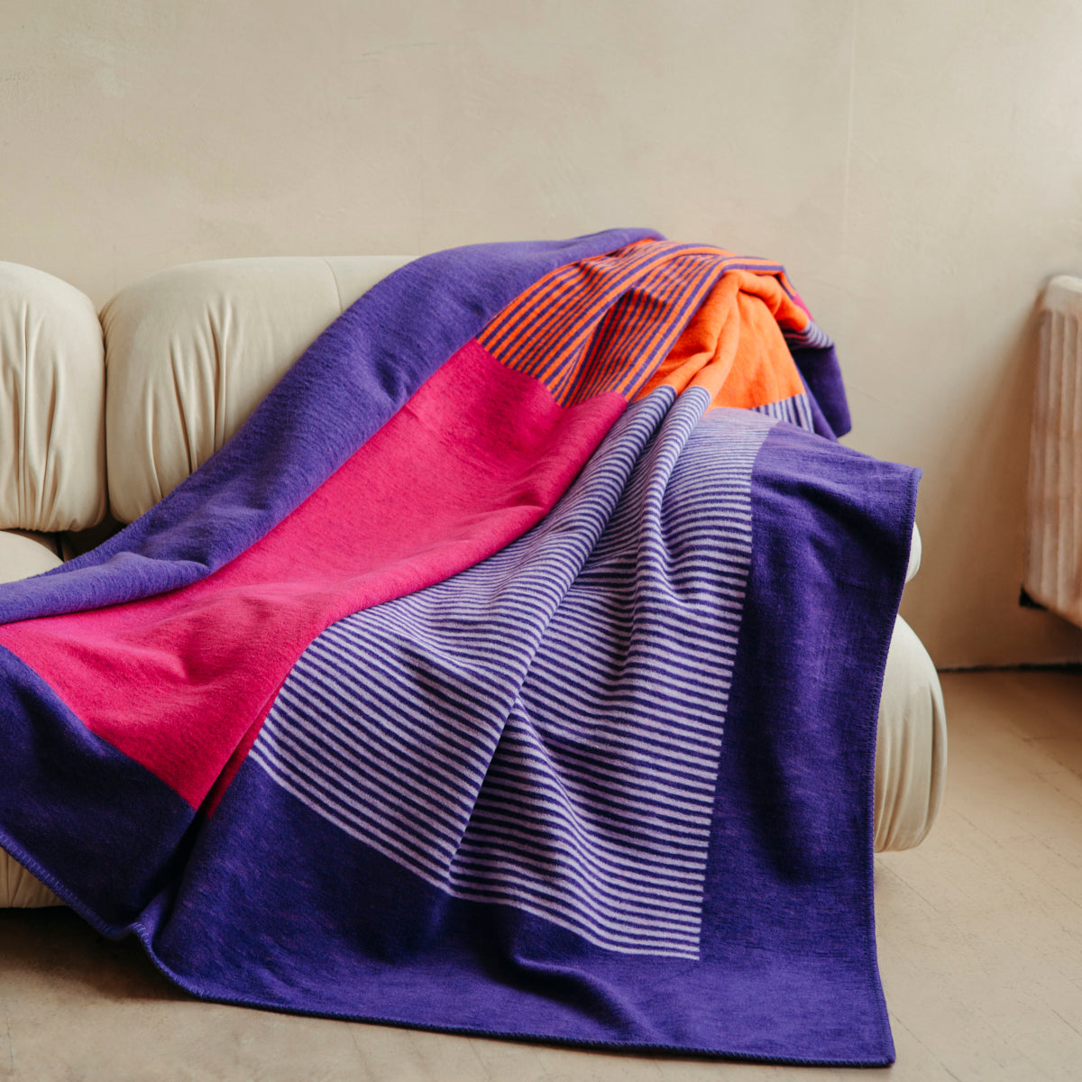 Blanket in bright purple, pink, and orange asymmetrical designs, draped over sofa.