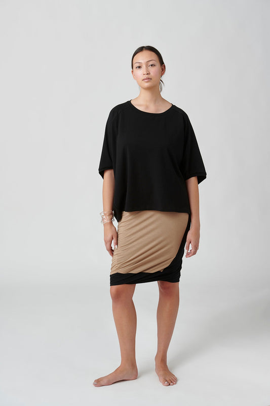 Front view of woman wearing black top and tan with black accent skirt.