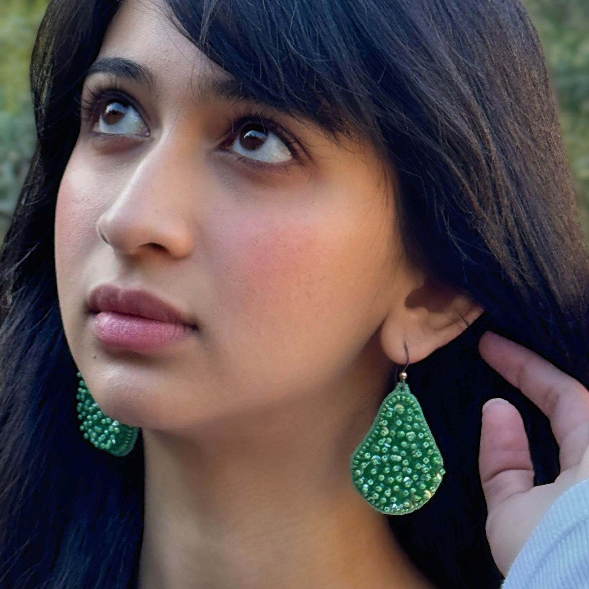 Left front view of woman looking up and wearing beaded pincushion green glass tassel earrings.