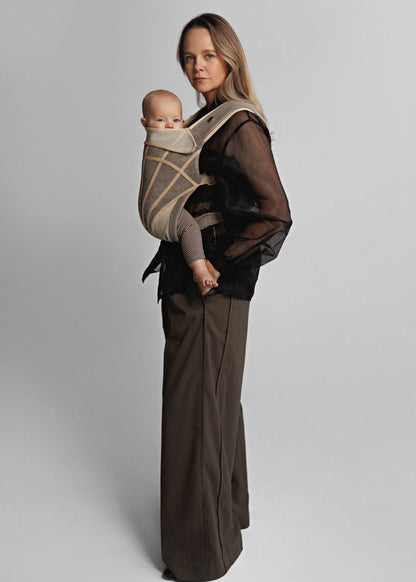 Side left view of Woman carrying baby on chest in a baby carrier. Woman is wearing black shirt and brown pants.