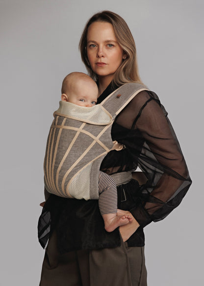 Closeup of Woman carrying baby on chest in a baby carrier that is grey with stripes. Woman is wearing black shirt and brown pants.