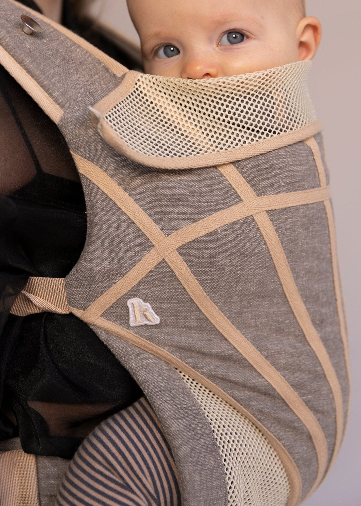 Closeup of baby in grey with tan stripes baby carrier.